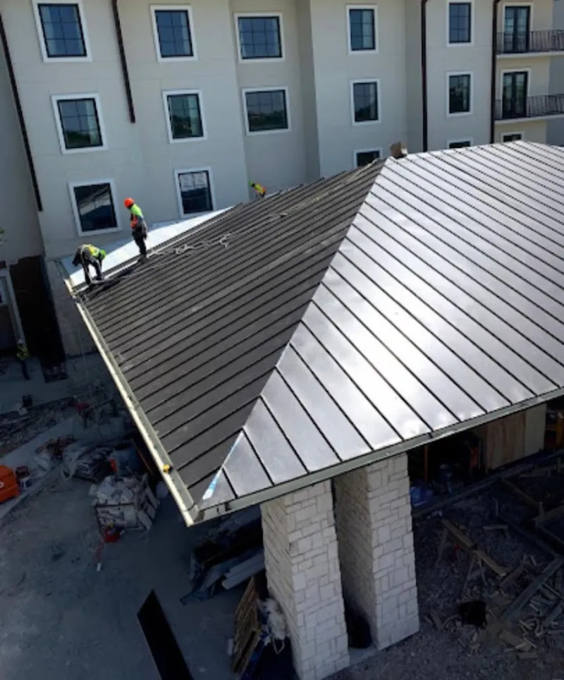 Crew installing standing seam metal roof panels on a commercial project in Leoni